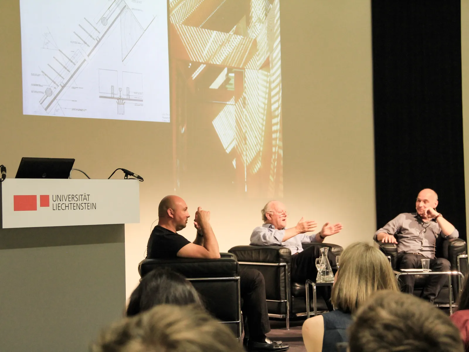 Drei Männer sitzen in Sesseln auf dem Podium und diskutieren