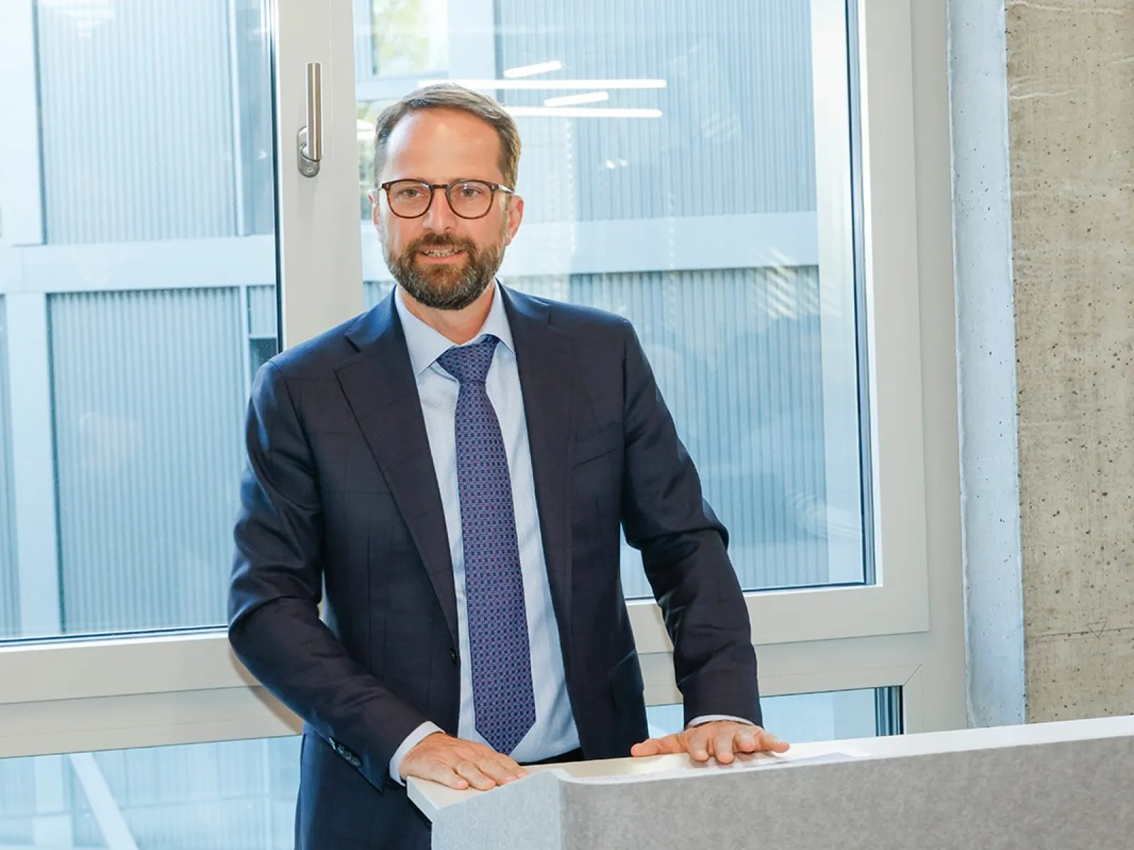 Ein Mann im Anzug steht an einem Rednerpult vor einem Fenster.