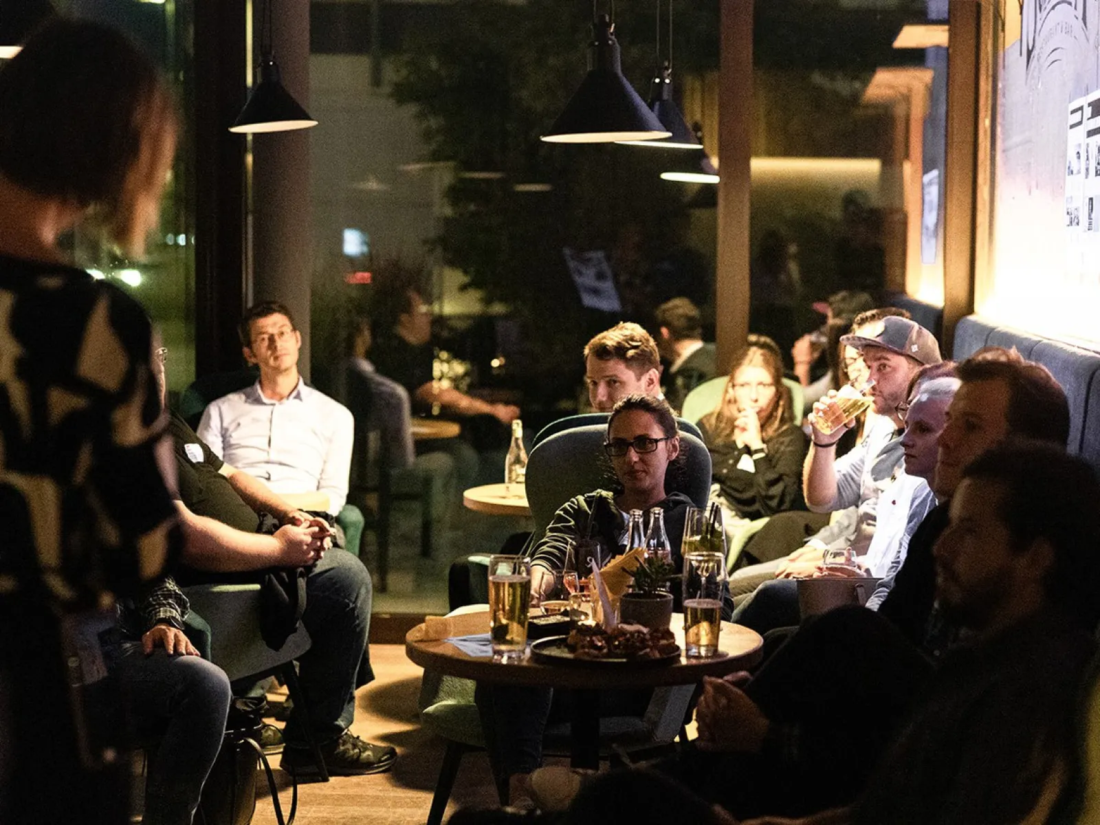Alumni-Treffen in gemütlicher Atmosphäre: Eine Gruppe von Menschen sitzt in einer Lounge, unterhält sich und genießt Getränke.