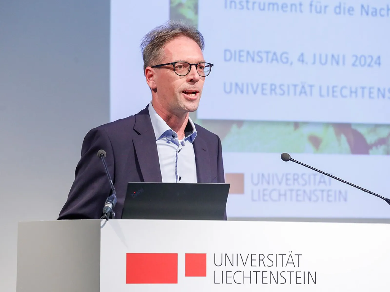 Ein Mann hält einen Vortrag im Auditorium der Universität Liechtenstein. Im Hintergrund ist eine Präsentation mit dem Datum 4. Juni 2024 zu sehen. Ein Rednerpult mit dem Logo der Universität steht vor ihm.