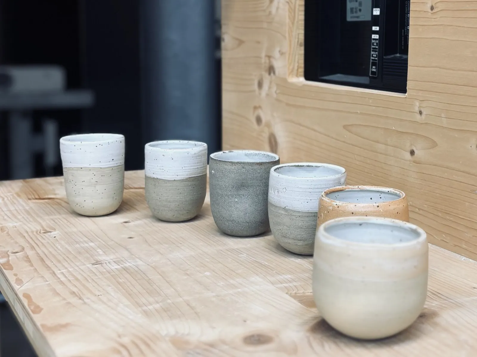 Sechs handgetöpferte Keramiktassen in verschiedenen Erdtönen stehen auf einem Holztisch. Die Tassen sind schlicht und modern gestaltet, passend zur Architekturveranstaltung an der Universität Liechtenstein.