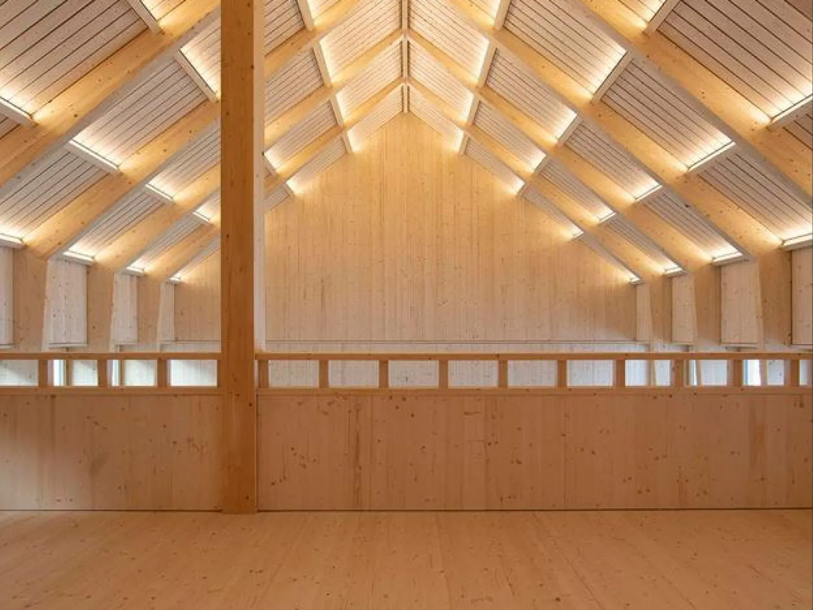 Innenansicht eines modernen Holzgebäudes mit sichtbarer Dachkonstruktion und natürlicher Beleuchtung. Die Architektur betont klare Linien und nachhaltige Materialien.