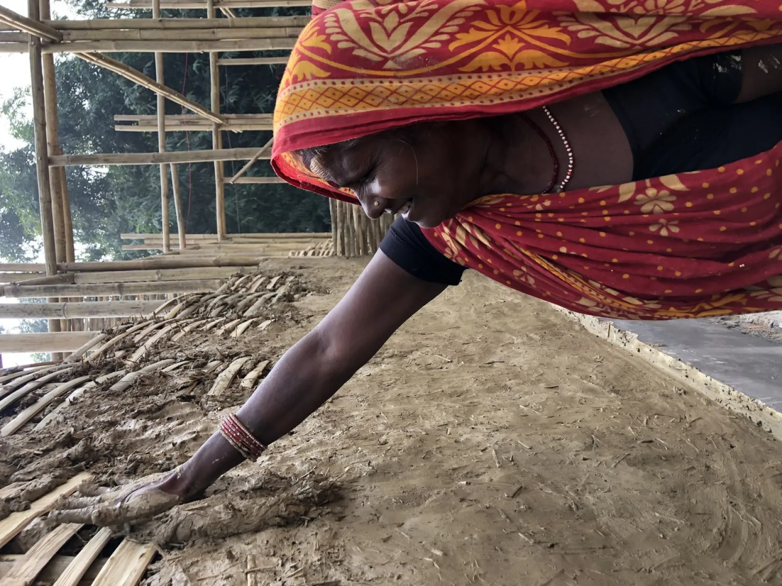 Frau verputzt mit Lehm eine Bambuswand für nachhaltiges Bauprojekt in Südasien