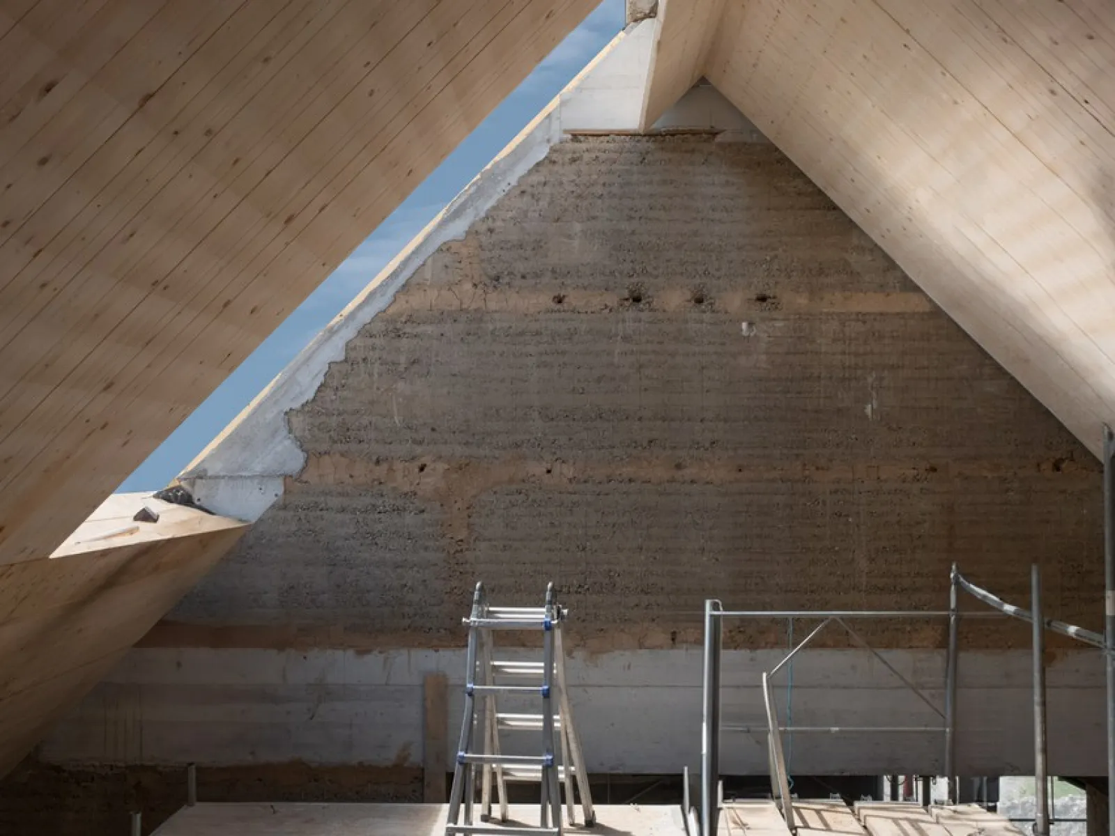 Innenansicht eines Dachbodens in Renovierung mit sichtbarer Holzkonstruktion und Gerüst. Natürliches Licht fällt durch ein Dachfenster.
