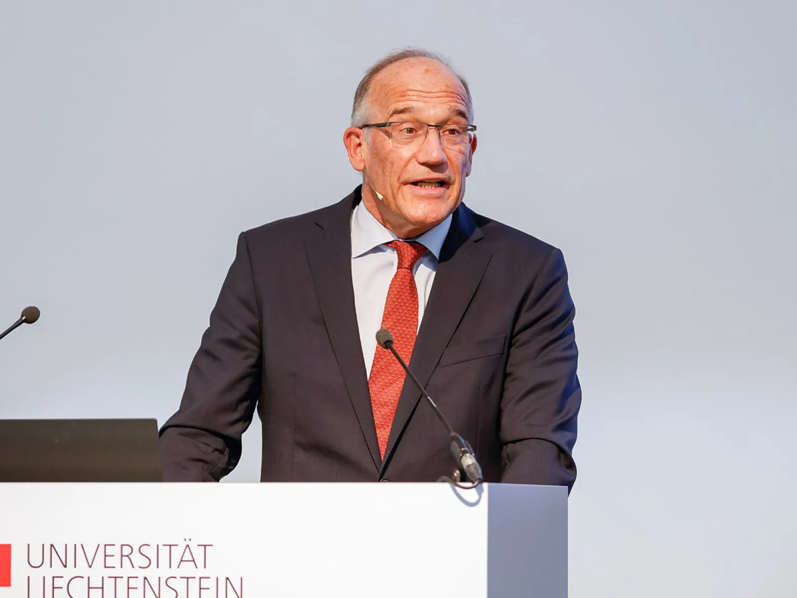 Ein Redner im Anzug steht am Podium der Universität Liechtenstein und hält eine Präsentation.