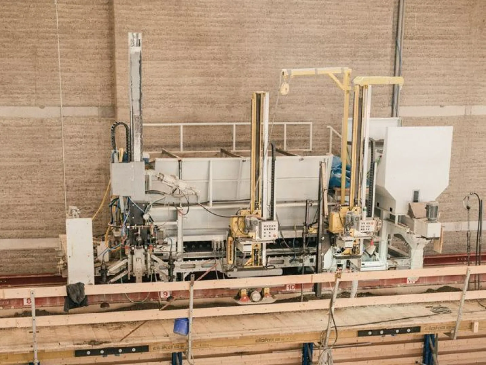Produktionshalle für Lehmbau mit Maschinen und Holzstrukturen, die den Bauprozess veranschaulichen.