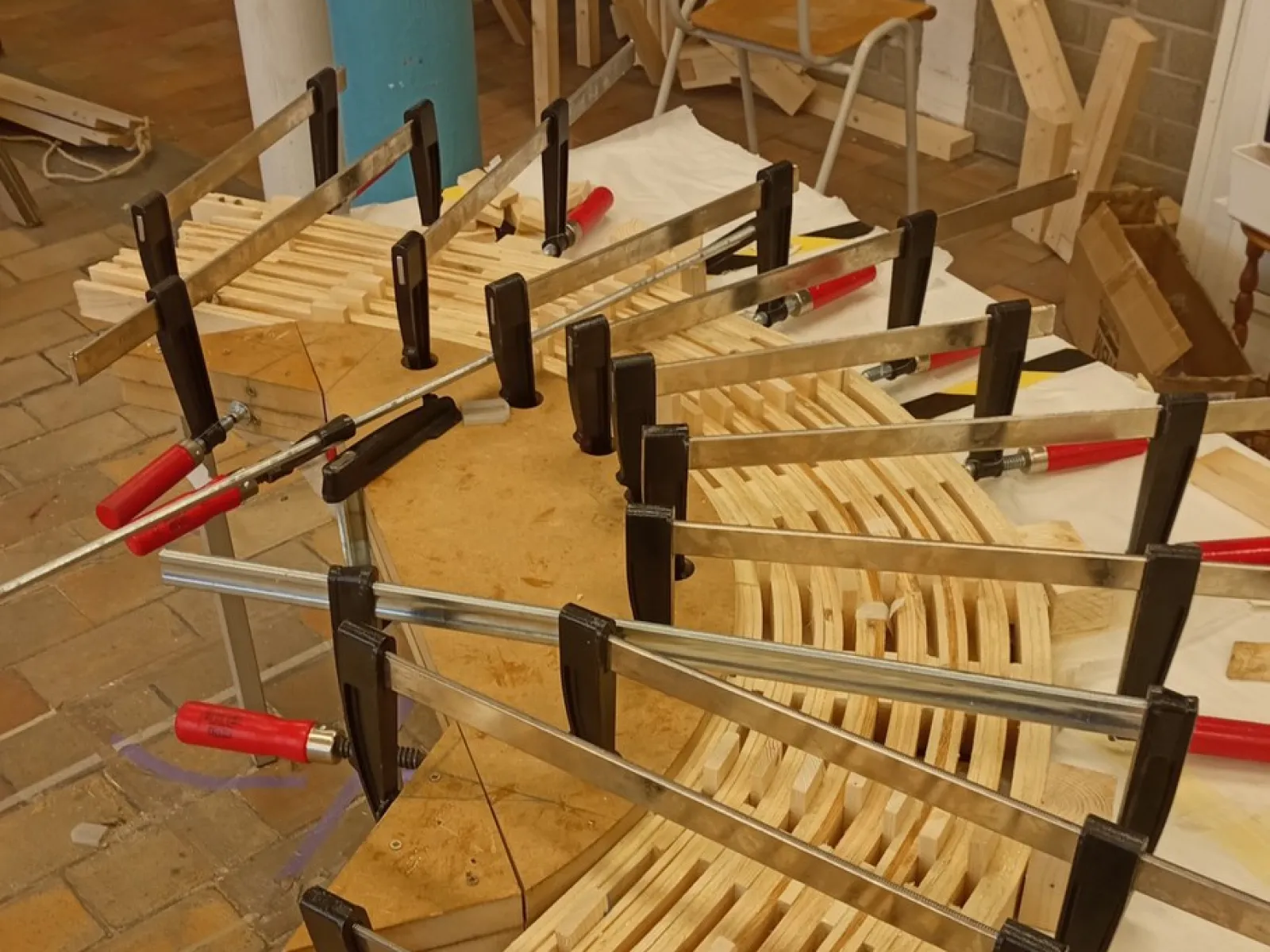 Ein Holzmodell eines Möbelstücks wird mit mehreren Schraubzwingen auf einem Tisch fixiert. Das Bild zeigt den handwerklichen Prozess der Studierenden während der «Maak Week» an der Universität Antwerpen.