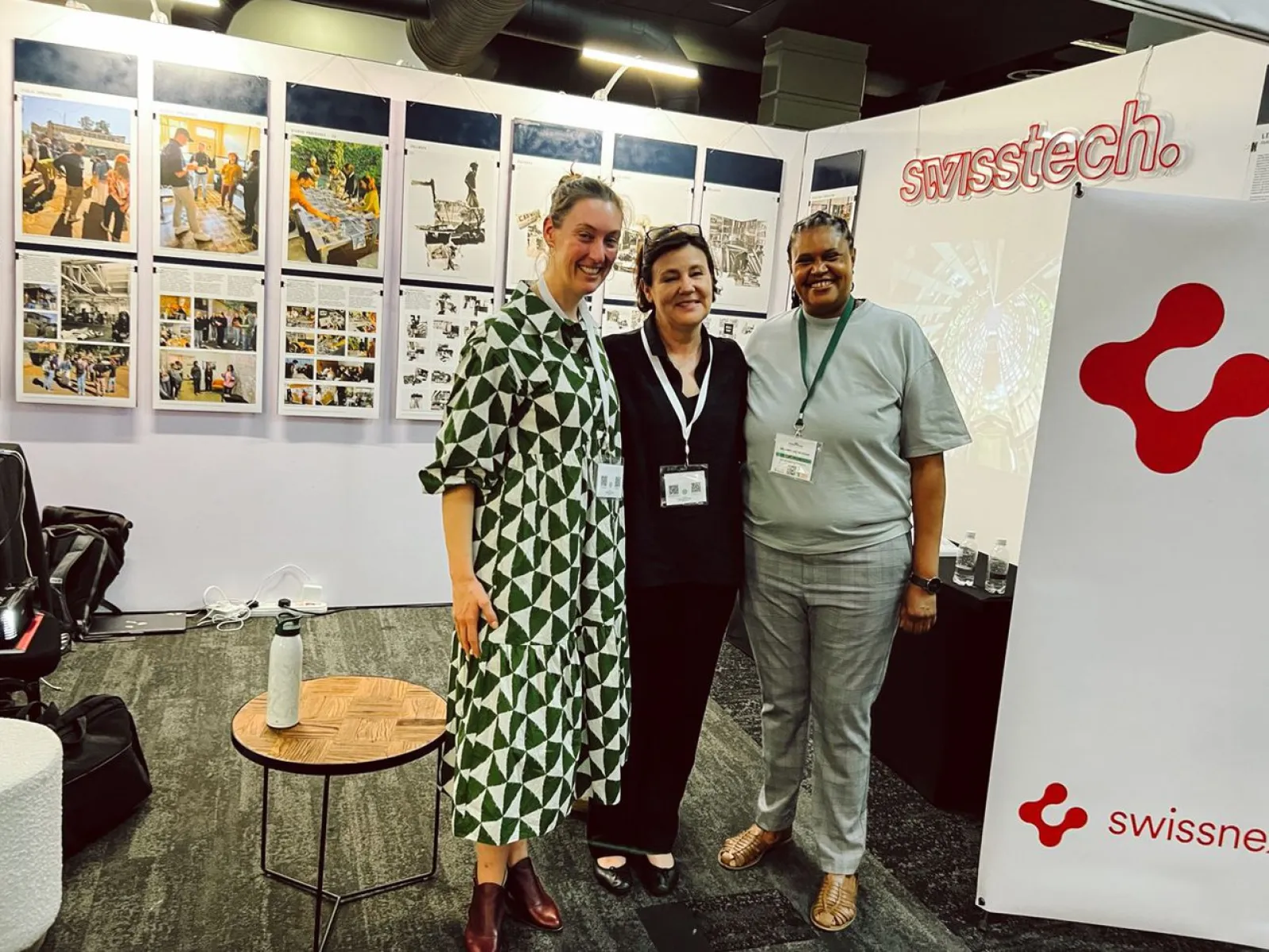 Drei Personen stehen lächelnd vor Ausstellungstafeln mit Bildern und Texten. Im Hintergrund ist ein Banner mit dem Logo von "swisstech" zu sehen. Die Szene befindet sich in einem Ausstellungsraum, der Teil der Präsentation "Making Urban Africa" auf dem South African Science Forum ist.