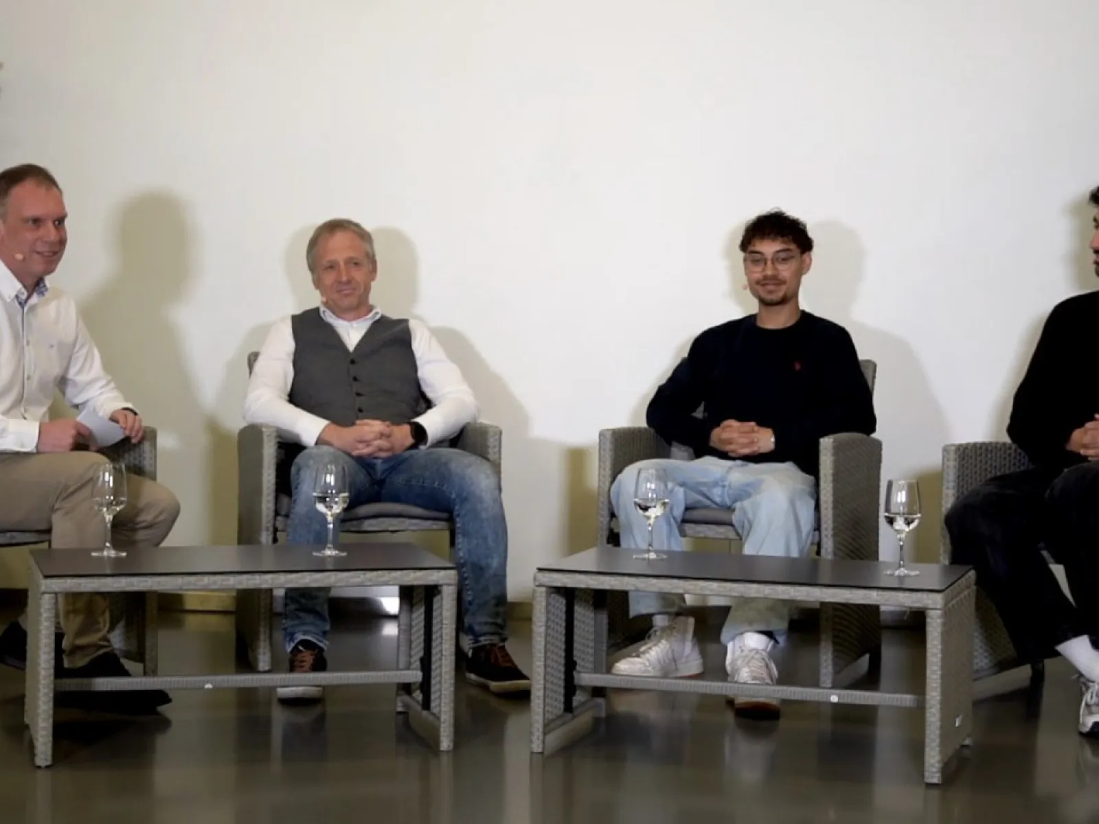 Vier Männer sitzen in einer Gesprächsrunde auf grauen Sesseln. Vor ihnen stehen zwei niedrige Tische mit Wassergläsern. Im Hintergrund sind Pflanzen zu sehen. Oben rechts befindet sich das Logo des Campus Radio der Universität Liechtenstein.