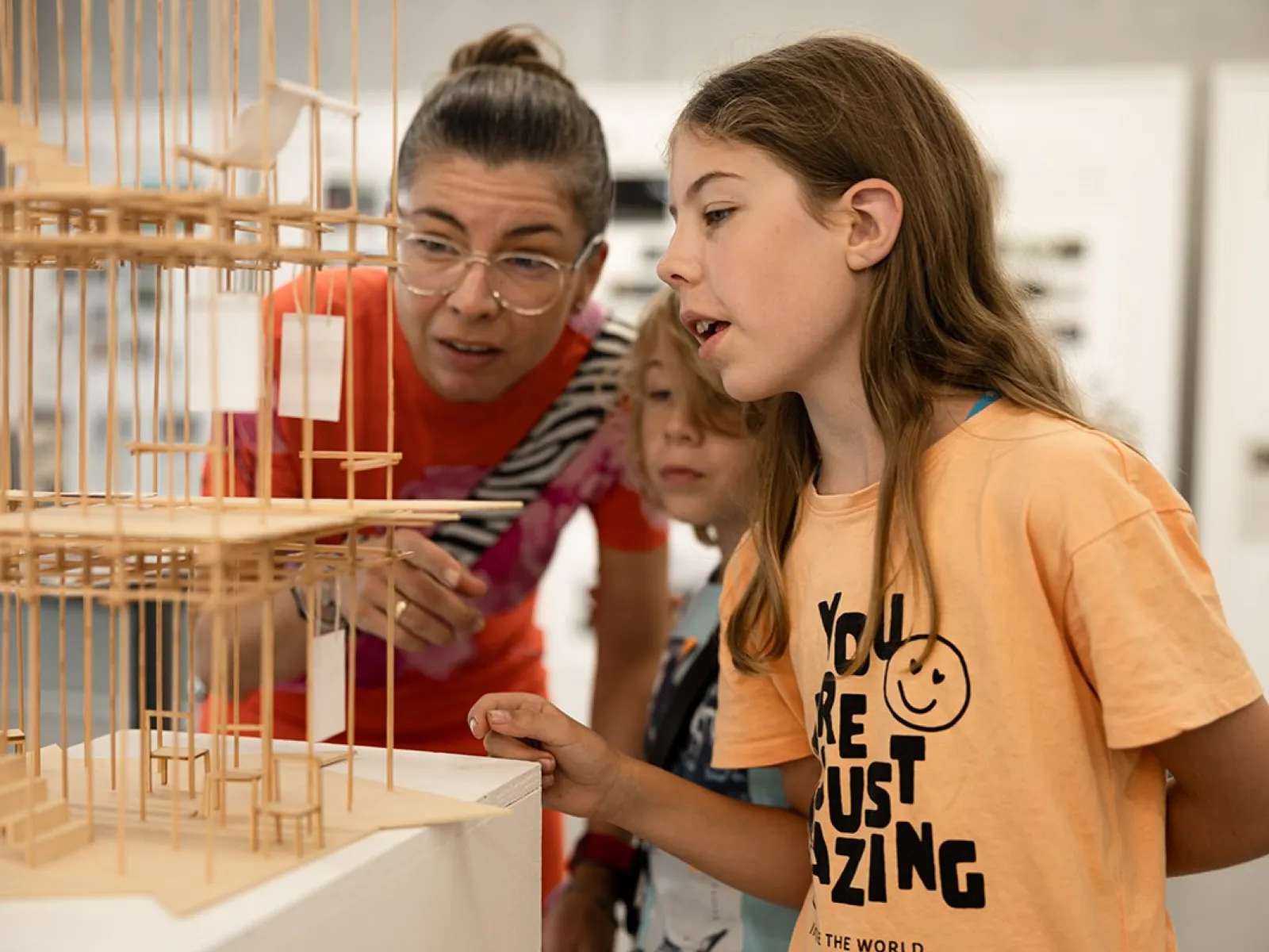 Eine Frau und zwei Kinder betrachten ein detailliertes Architekturmodell aus Holz. Die Szene findet in einem Ausstellungsraum statt, der Teil des Tags der offenen Tür an der Universität Liechtenstein ist.