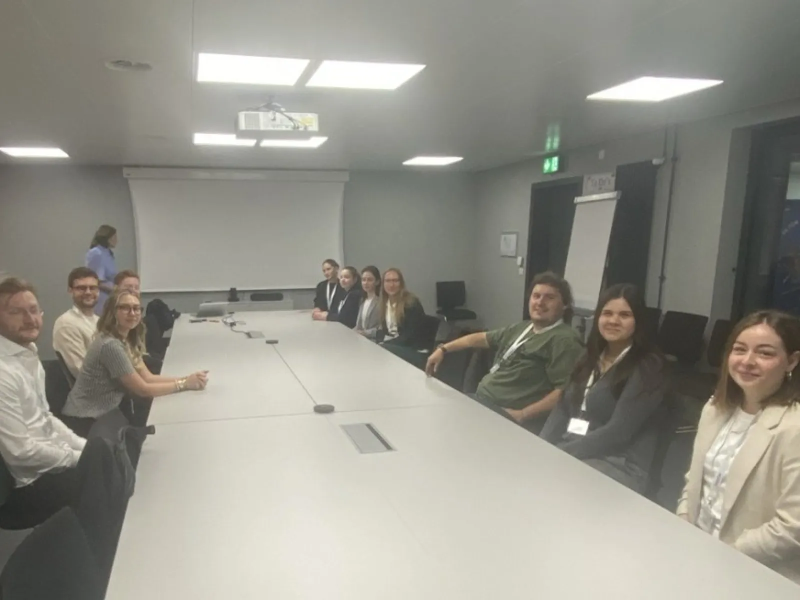 Studierende der Universität Liechtenstein sitzen in einem Konferenzraum bei Ivoclar in Schaan. Im Hintergrund ist eine Präsentationsleinwand zu sehen.