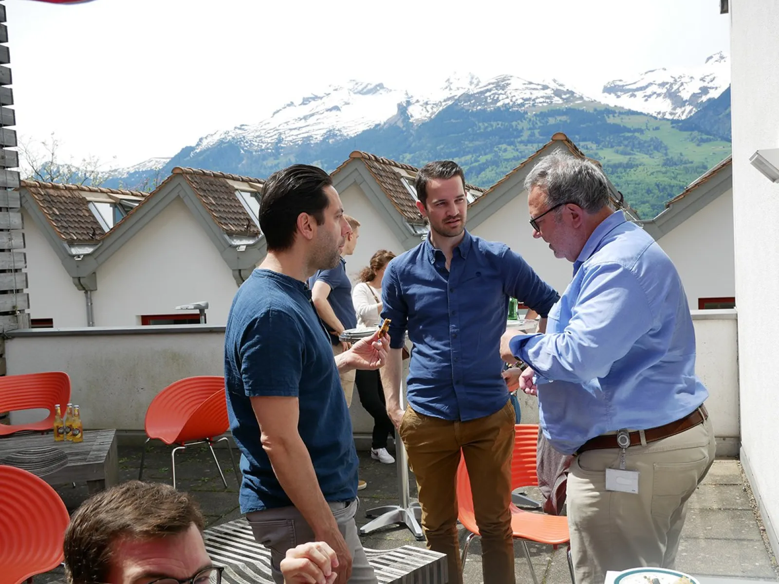 Alumni-Treffen an der Universität Liechtenstein: Ehemalige Studierende unterhalten sich auf einer sonnigen Terrasse mit Bergblick im Hintergrund.