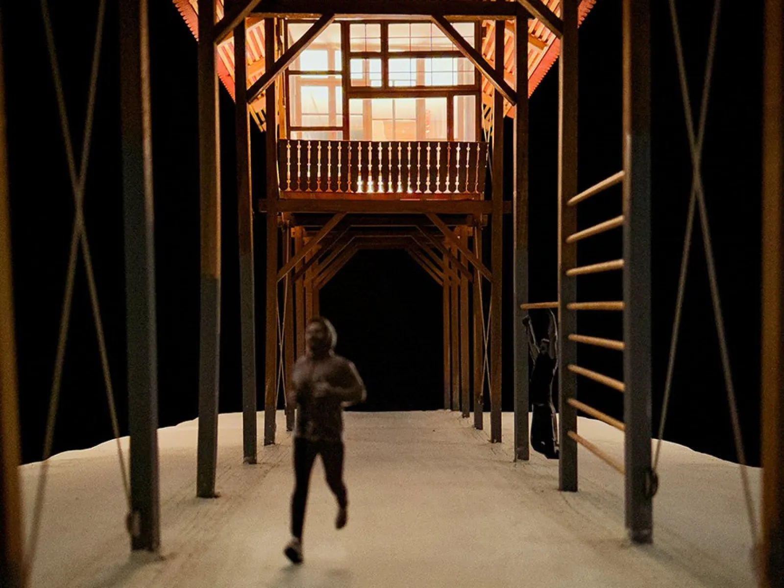 Ein Modell eines architektonischen Entwurfs zeigt eine überdachte Struktur mit sichtbaren Holzbalken. Eine Person läuft auf einem Weg unter der Konstruktion. Das Design kombiniert traditionelle Bauweise mit modernen Elementen und betont lineare Formen.