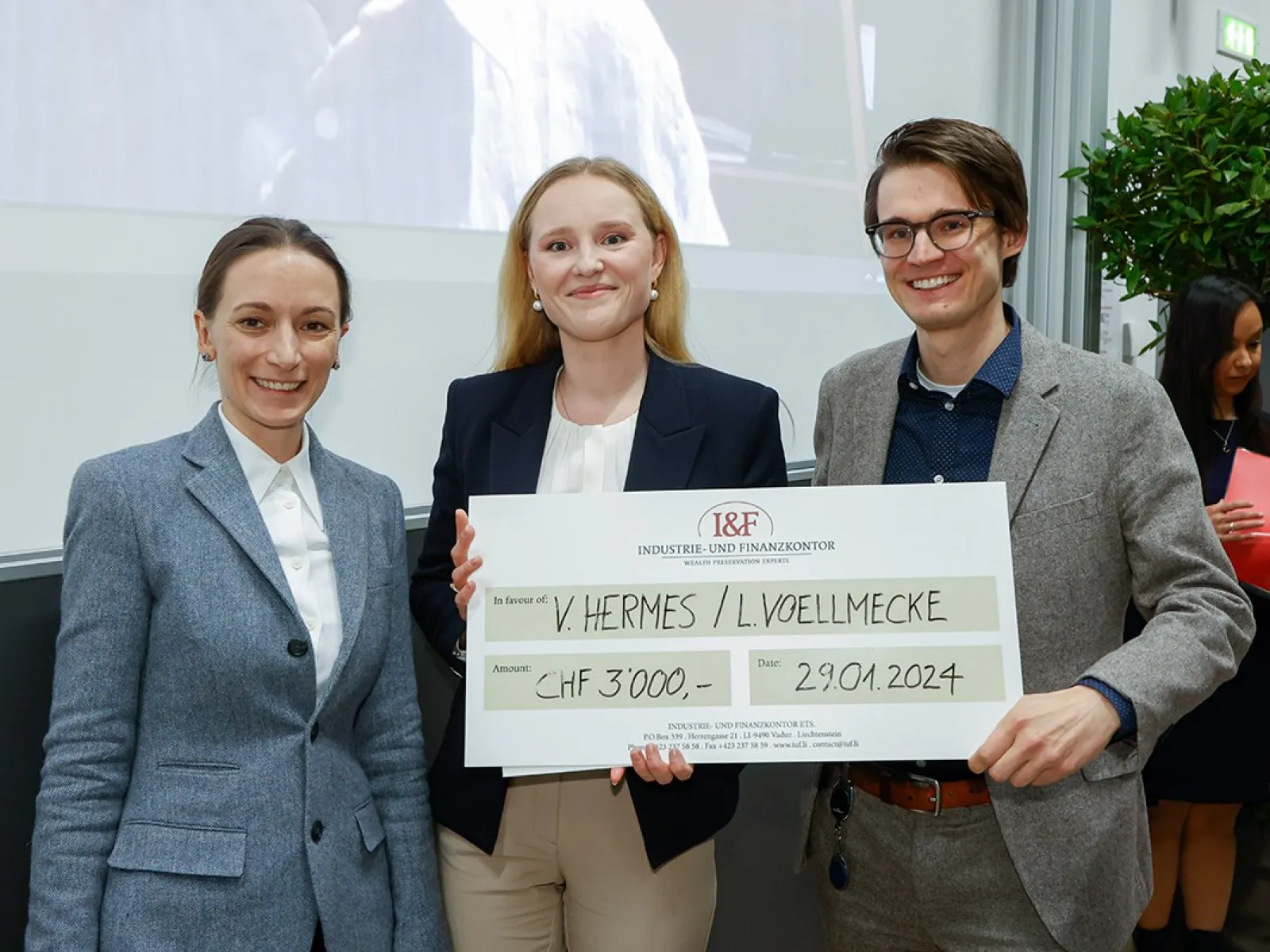 Drei Personen halten einen großen Scheck mit der Aufschrift "I&F Family Wealth Preservation Award" in einem Veranstaltungsraum. Sie lächeln in die Kamera.
