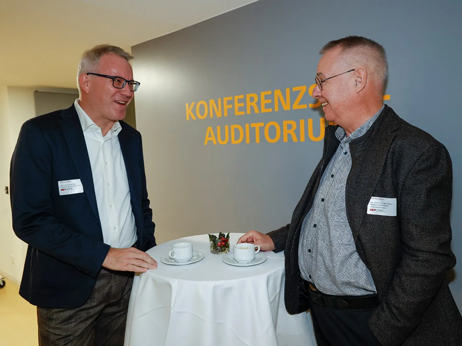 Zwei Männer im Gespräch bei einer Veranstaltung an der Universität Liechtenstein. Sie stehen an einem Stehtisch mit Kaffeetassen im Bereich "Konferenzzentrum Auditorium".