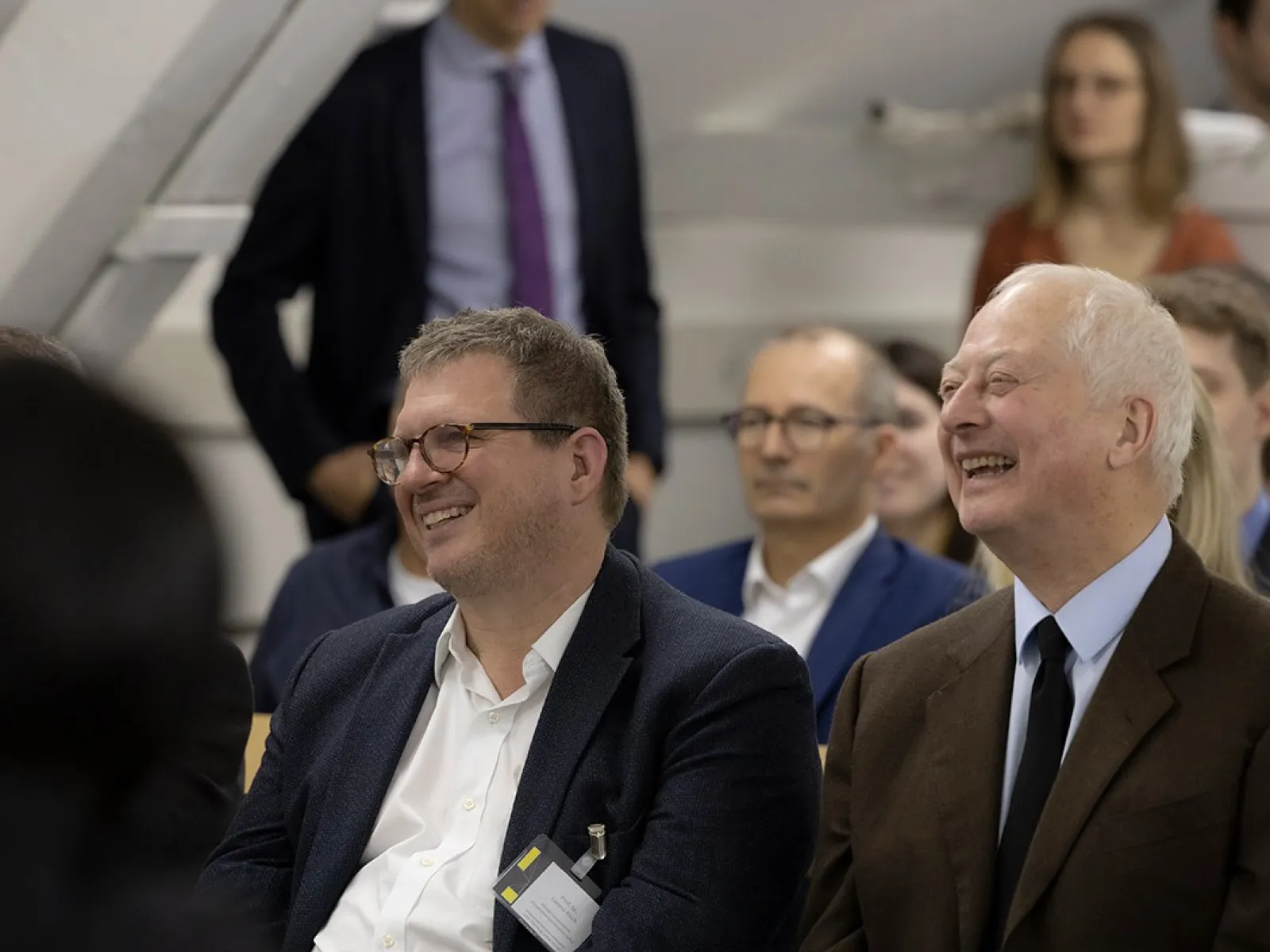 Teilnehmer einer Podiumsdiskussion an der Universität Liechtenstein, lächelnd und aufmerksam, in einem gut besuchten Veranstaltungsraum.