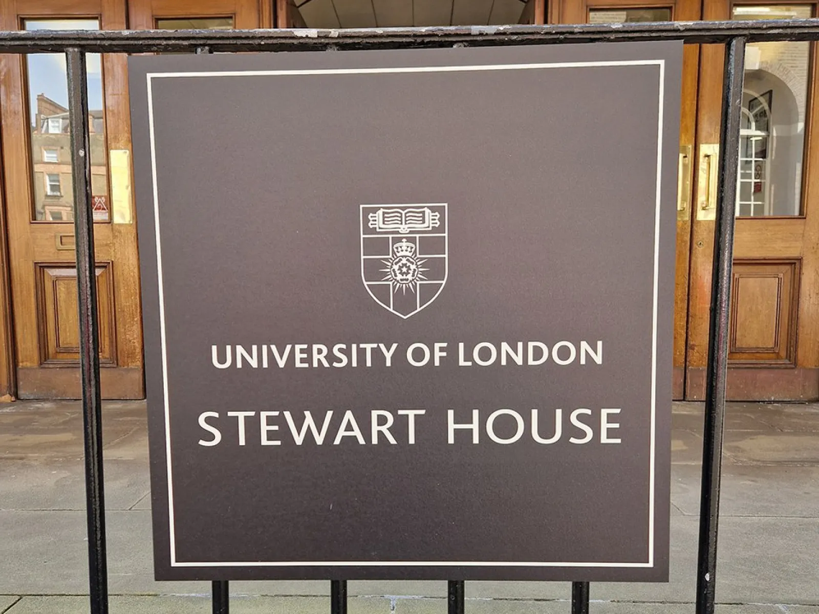 Ein Schild vor dem Eingang eines Gebäudes mit der Aufschrift "University of London, Stewart House". Im Hintergrund sind Holztüren und die Hausnummer 32 zu sehen.