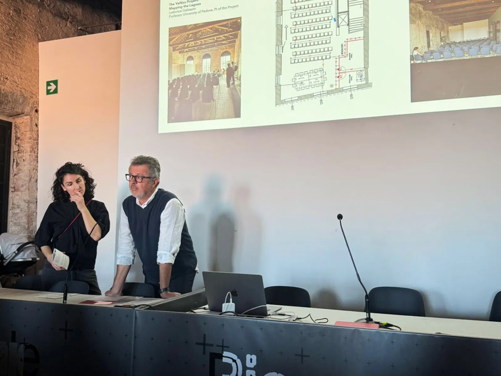 Zwei Personen tragen etwas vor mit einer Beamerprojektion im Hintergrund