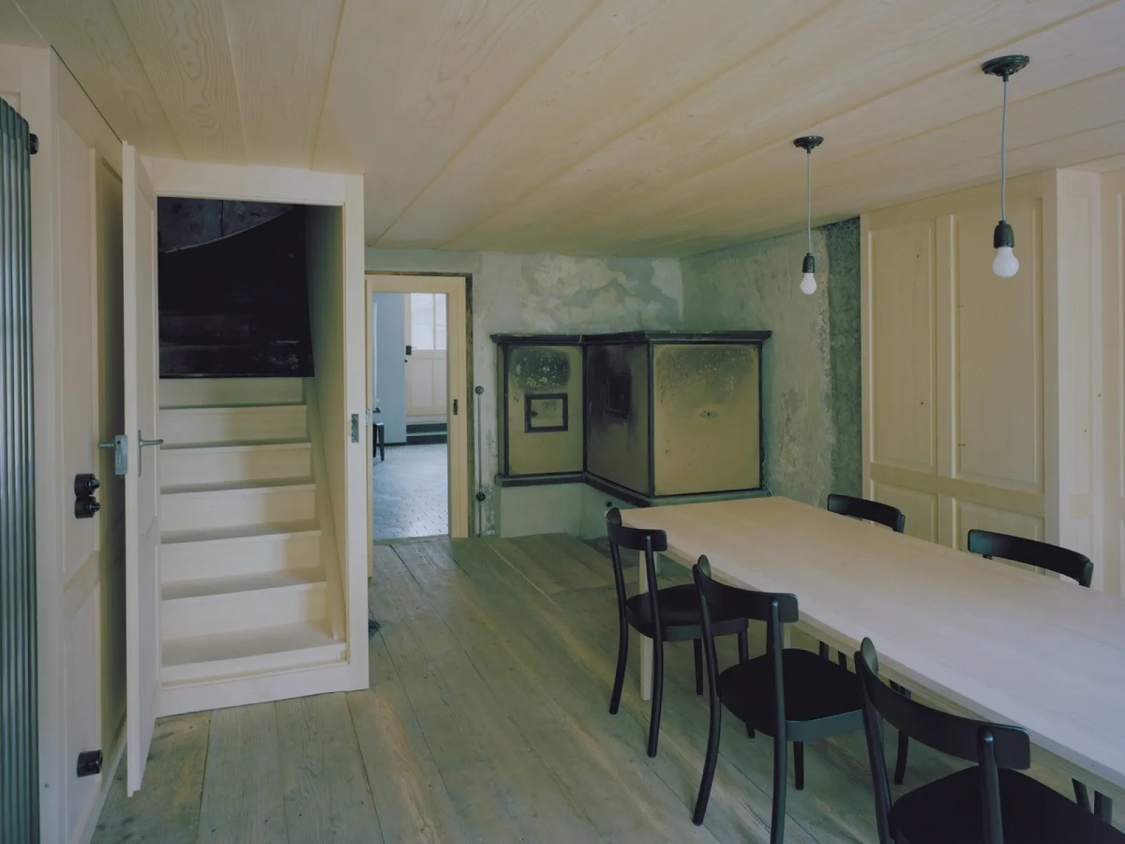Minimalistischer Innenraum mit Holztisch und historischem Ofen in renoviertem Gebäude
