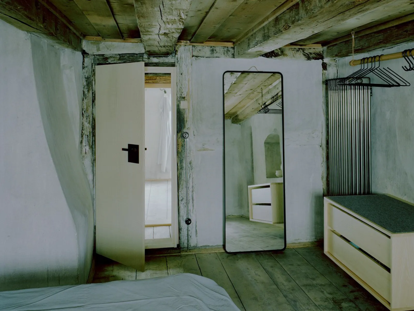 Rustikales Schlafzimmer mit Holzbalkendecke, Spiegel und schlichten Möbeln in renoviertem Altbau