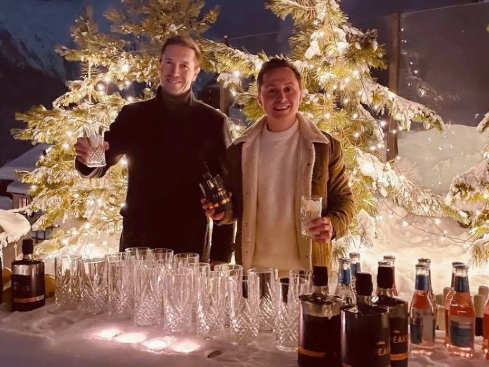 Winterliche Outdoor Bar mit Getränken und zwei Personen vor beleuchtetem Weihnachtsbaum bei Networking Event