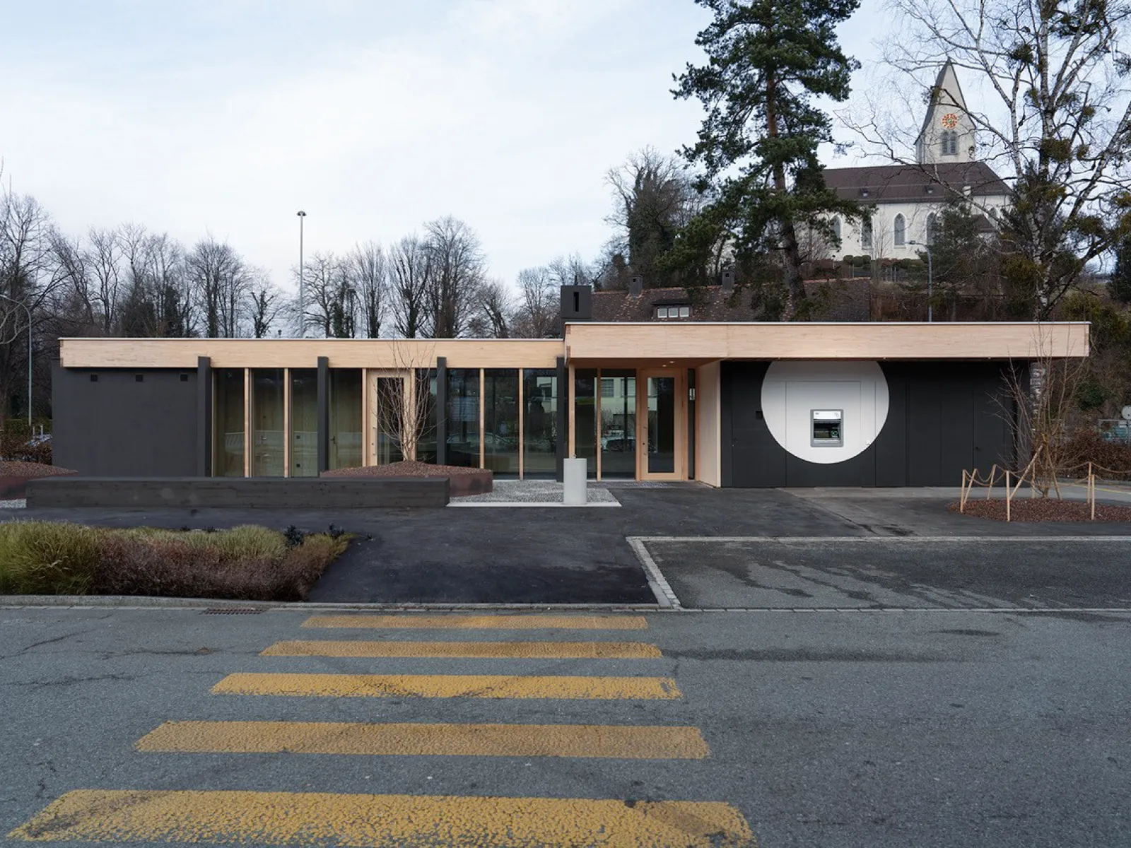 Zeitgenössisches Flachbau Gebäude mit klarer Linienführung vor Kirche und Strassenraum Architekturaufnahme