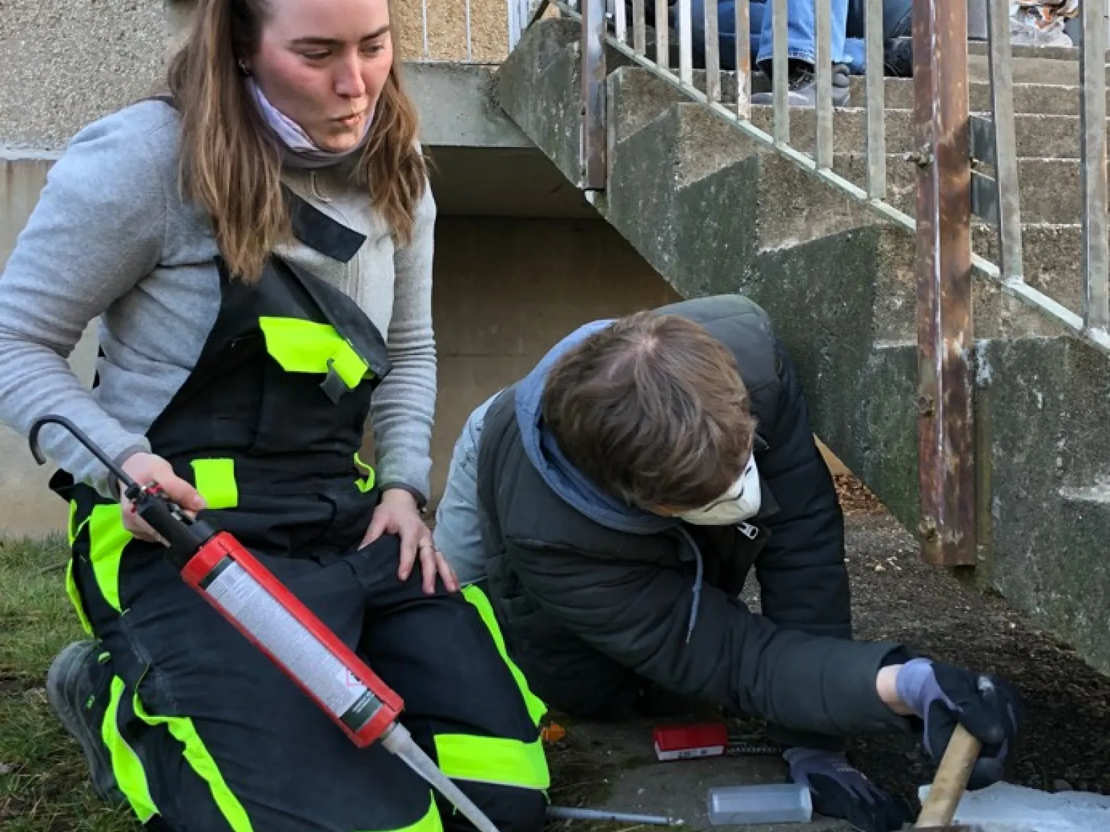 Zwei junge Leute in Arbeiterkleidung arbeiten an einer Aussentreppe