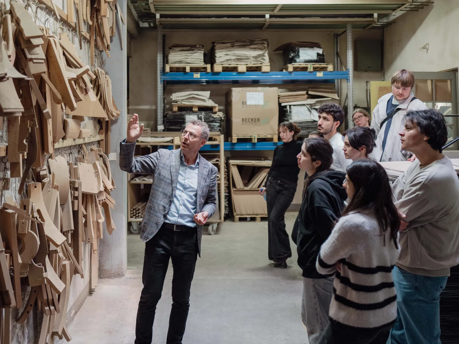Mann zeigt auf eine Wand mit Holzvorlagen und erklärt sie einer Gruppe von Studierenden 