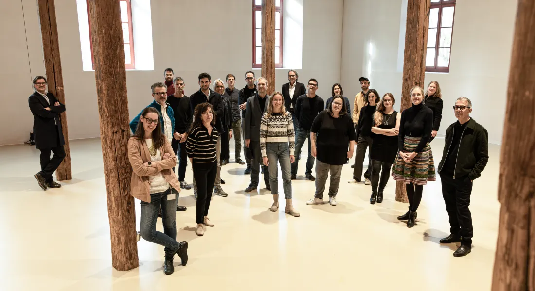 Eine Gruppe von Menschen steht in einer Halle und blickt in die Kamera. 