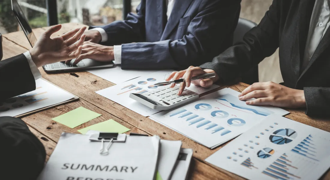 mehrere Personen sitzen gemeinsam an einem Tisch und arbeiten an zahlreichen Unterlagen