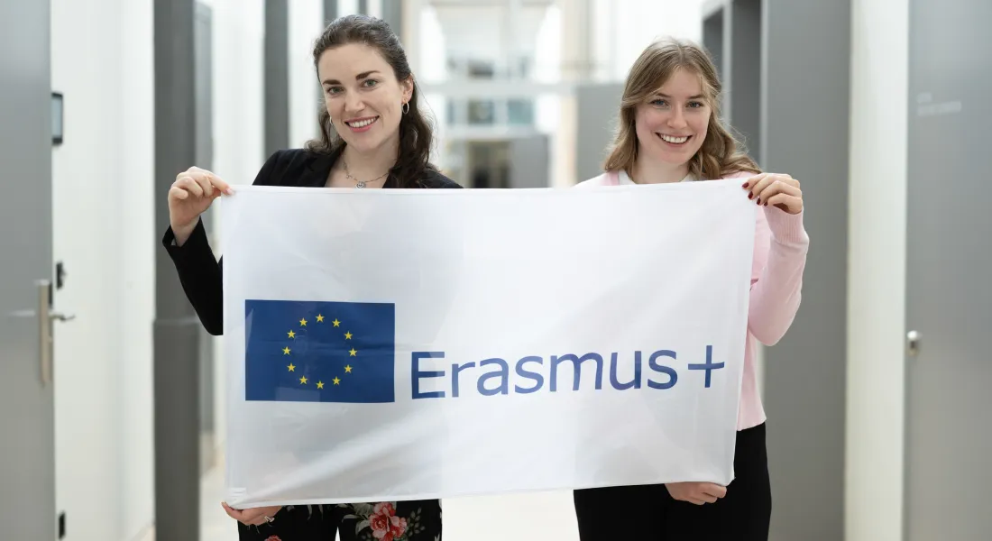Zwei Studentinnen halten Erasmus-Plus-Flagge im Uni-Gebäude.
