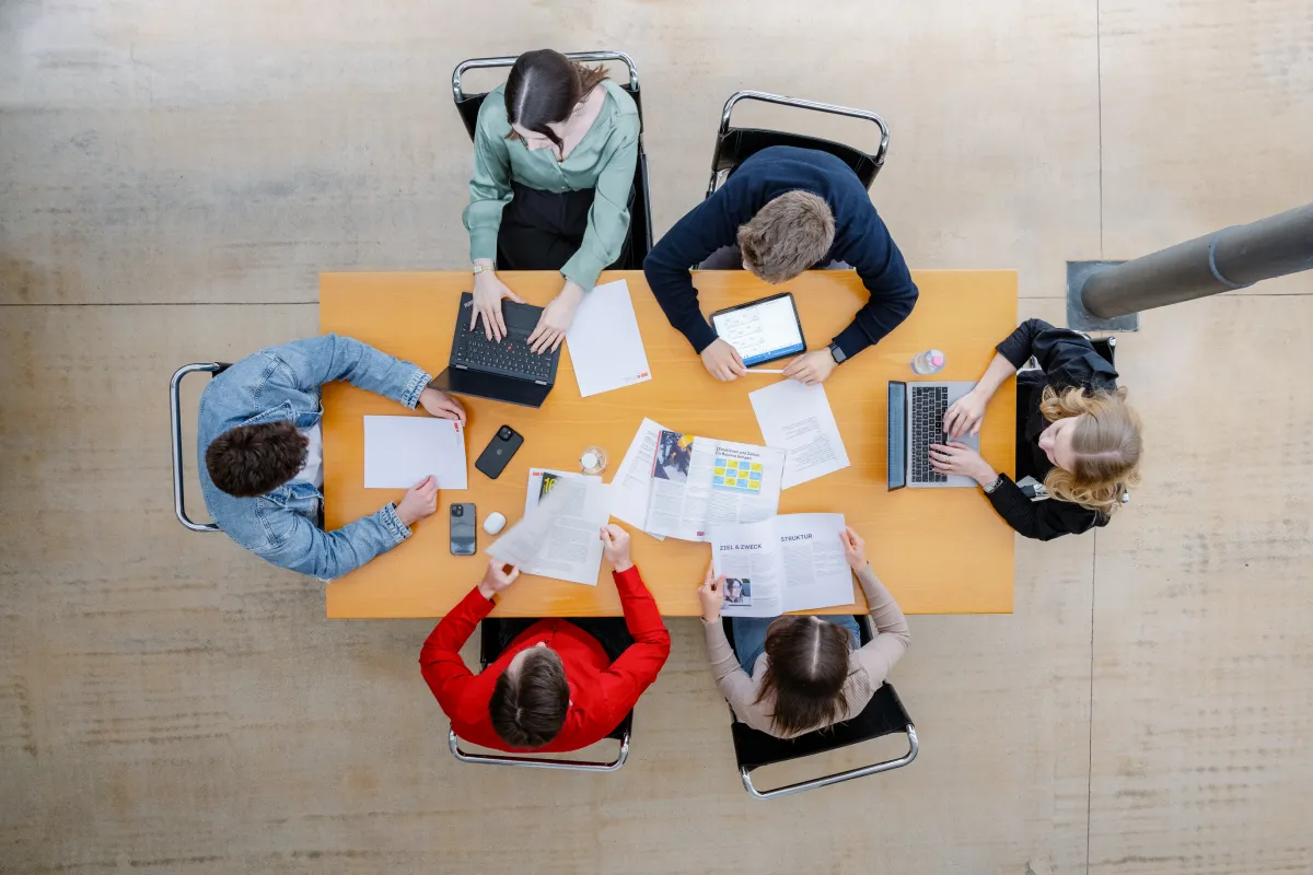 Studierende der Universität Liechtenstein arbeiten an einem Gruppentisch mit Laptops und Unterlagen im modernen Lernbereich.