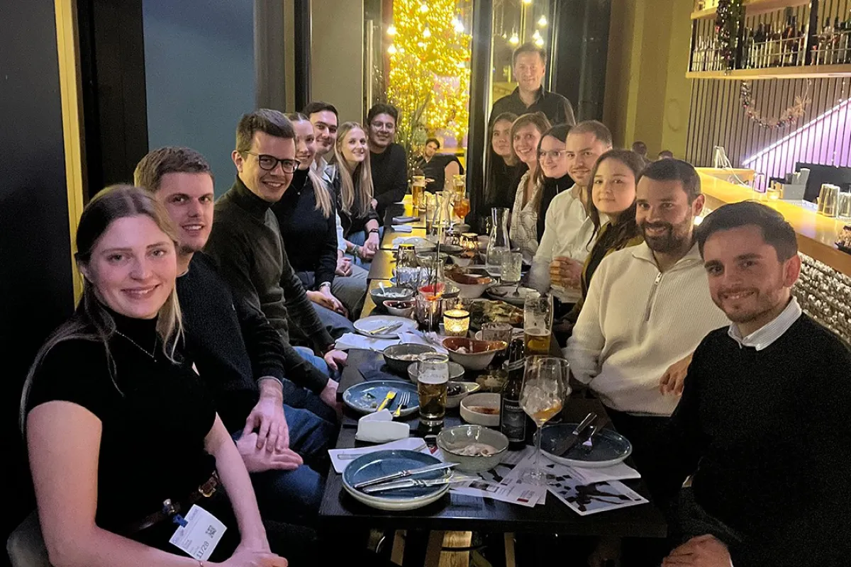 Eine Gruppe von Alumni der Universität Liechtenstein sitzt in einem Restaurant an einem langen Tisch, lächelnd und in geselliger Runde. Auf dem Tisch stehen Getränke und Teller mit Speisen. Die Atmosphäre ist warm und einladend.