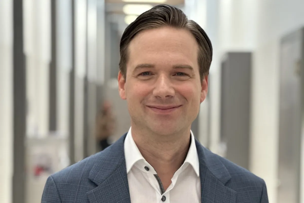 Ein lächelnder Mann in einem blauen Anzug steht in einem modernen, hellen Flur.