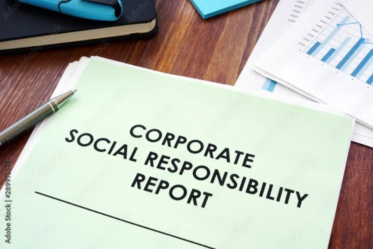Ein Dokument mit der Aufschrift "Corporate Social Responsibility Report" liegt auf einem Holztisch, daneben ein Stift und einige Diagramme.