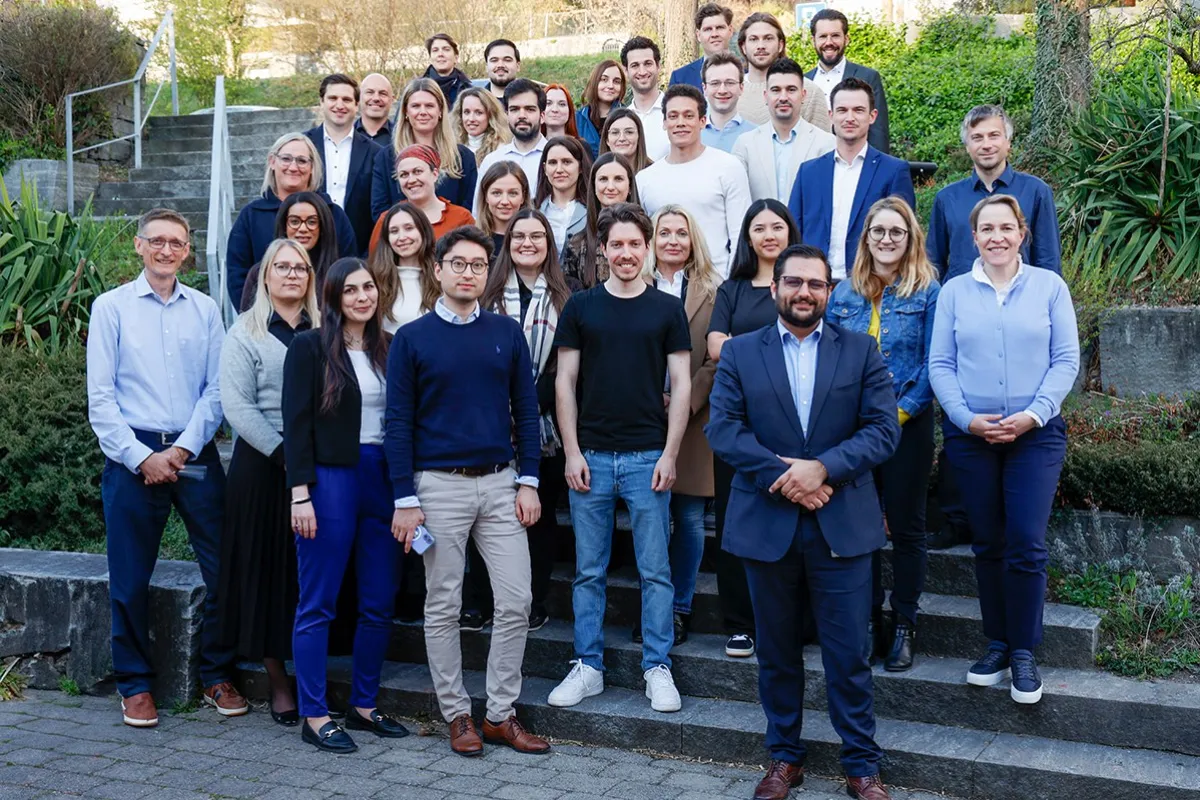 Gruppenfoto von Studierenden des Diplomstudiengangs Treuhandwesen an der Universität Liechtenstein, die auf einer Steintreppe im Freien stehen. Die Gruppe besteht aus Männern und Frauen in formeller Kleidung, umgeben von grüner Vegetation.