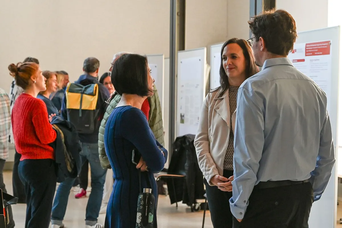 Menschen stehen in einem Auditorium der Universität Liechtenstein und unterhalten sich vor Ausstellungstafeln. Die Atmosphäre ist lebhaft, und die Veranstaltung scheint gut besucht zu sein.