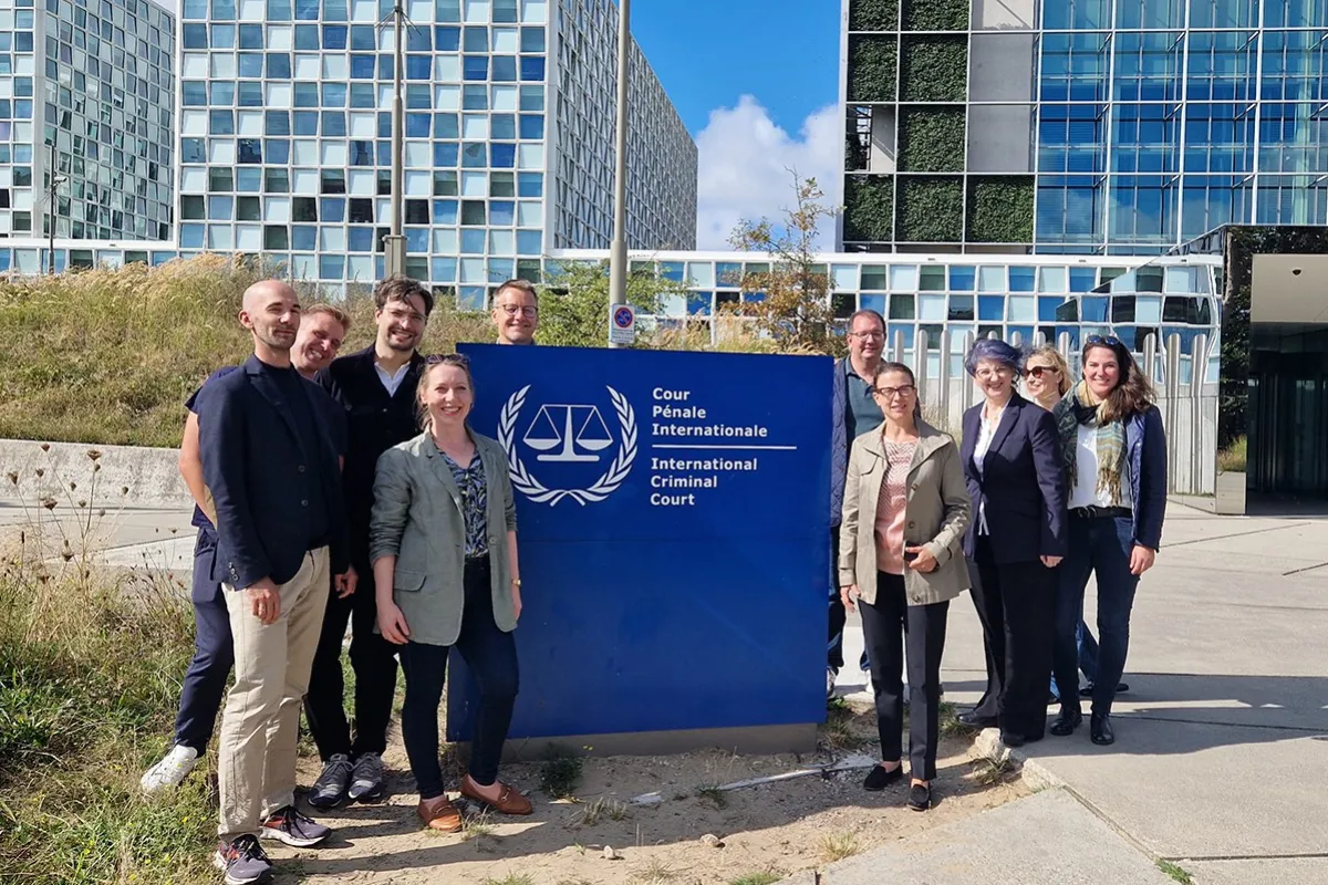 Gruppe von Studierenden des Executive Master of Laws (LL.M.) im Wirtschaftsstrafrecht vor dem Internationalen Strafgerichtshof in Den Haag, lächelnd und posierend vor dem Gebäude mit dem Logo des Gerichtshofs.