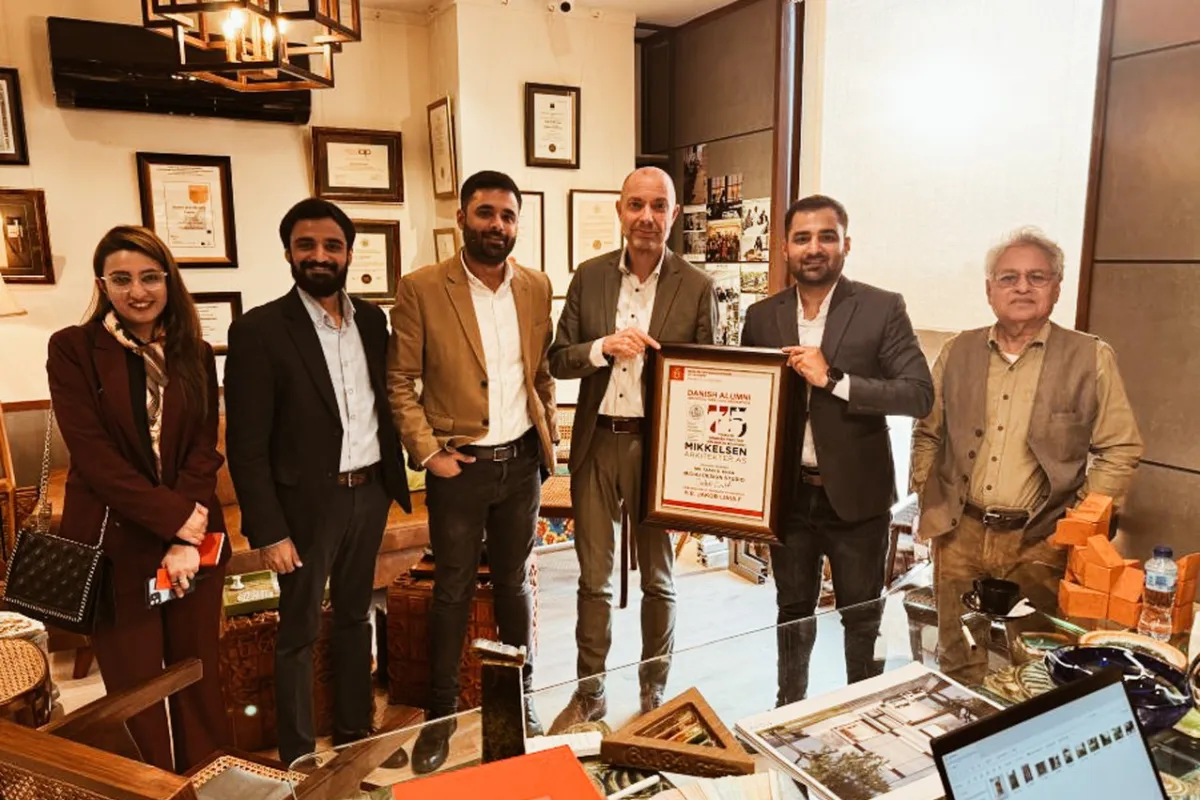 Eine Gruppe von sechs Personen steht in einem Büro, eine Person hält eine gerahmte Auszeichnung. Im Hintergrund sind Zertifikate und Auszeichnungen an der Wand zu sehen.