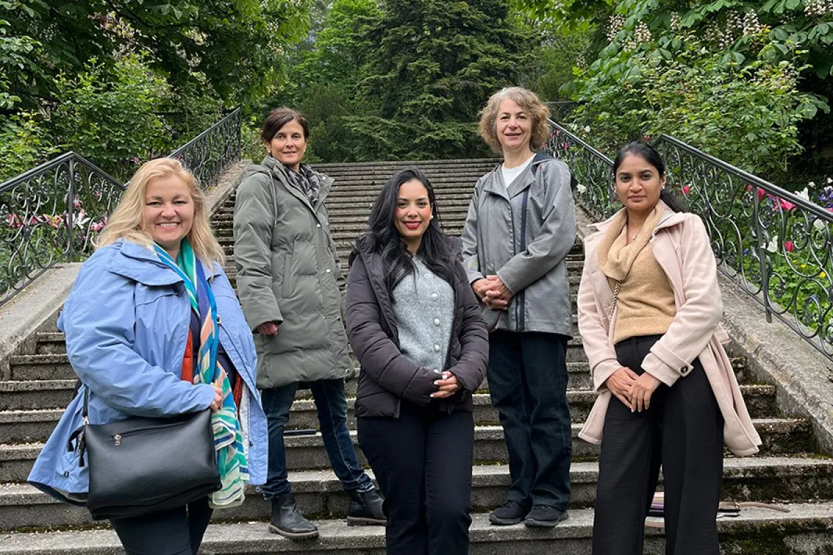Fünf Personen stehen auf einer Treppe im Freien, umgeben von grünen Bäumen. Sie lächeln in die Kamera.