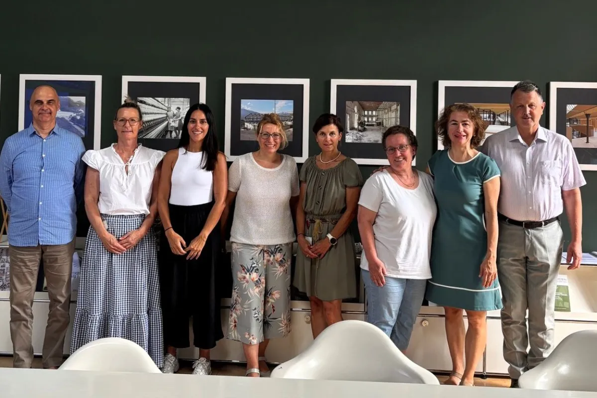 Eine Gruppe von acht Personen steht lächelnd vor einer Wand mit gerahmten Bildern. Sie befinden sich in einem Besprechungsraum der Universität Liechtenstein.