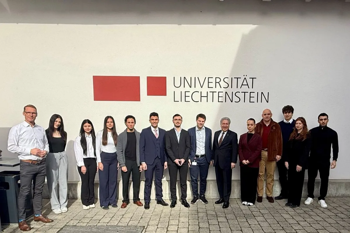 Eine Gruppe von Menschen steht vor einer Wand mit dem Logo der Universität Liechtenstein. Sie sind formell gekleidet und lächeln in die Kamera.
