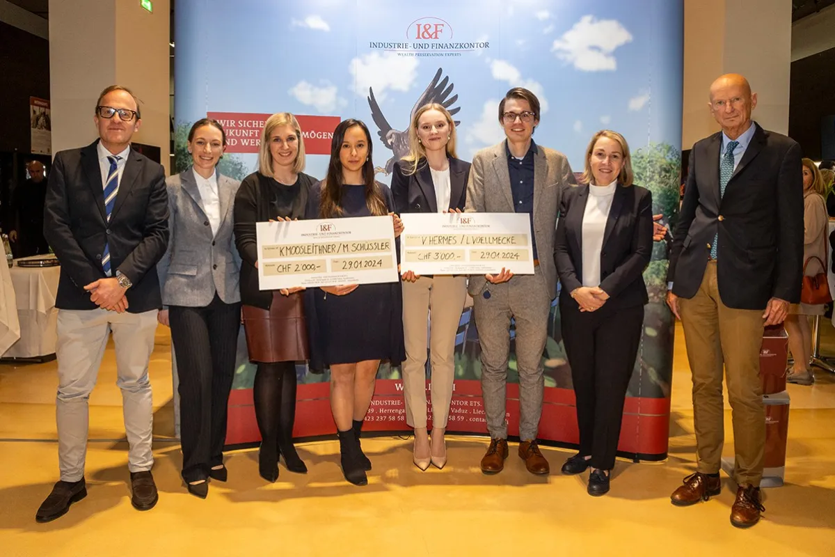 Gruppe von acht Personen posiert mit zwei großen Schecks bei der Verleihung des I&F Family Wealth Preservation Awards an der Universität Liechtenstein. Die Studierenden wurden für ihre herausragenden Strukturierungsvorschläge ausgezeichnet. Im Hintergrund ist ein Banner des Industrie- und Finanzkontors zu sehen.