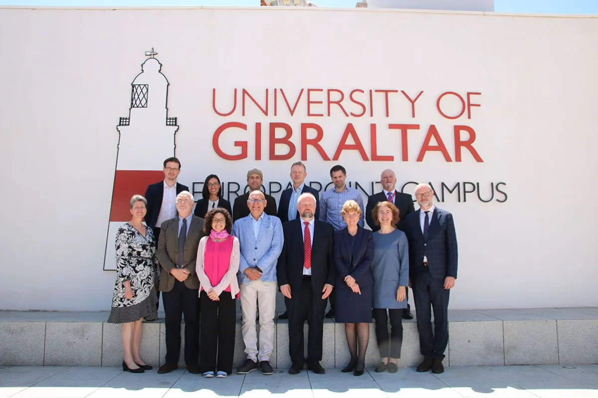 Eine Gruppe von Personen steht vor einem Gebäude mit der Aufschrift "University of Gibraltar". Sie posieren für ein Gruppenfoto bei sonnigem Wetter.