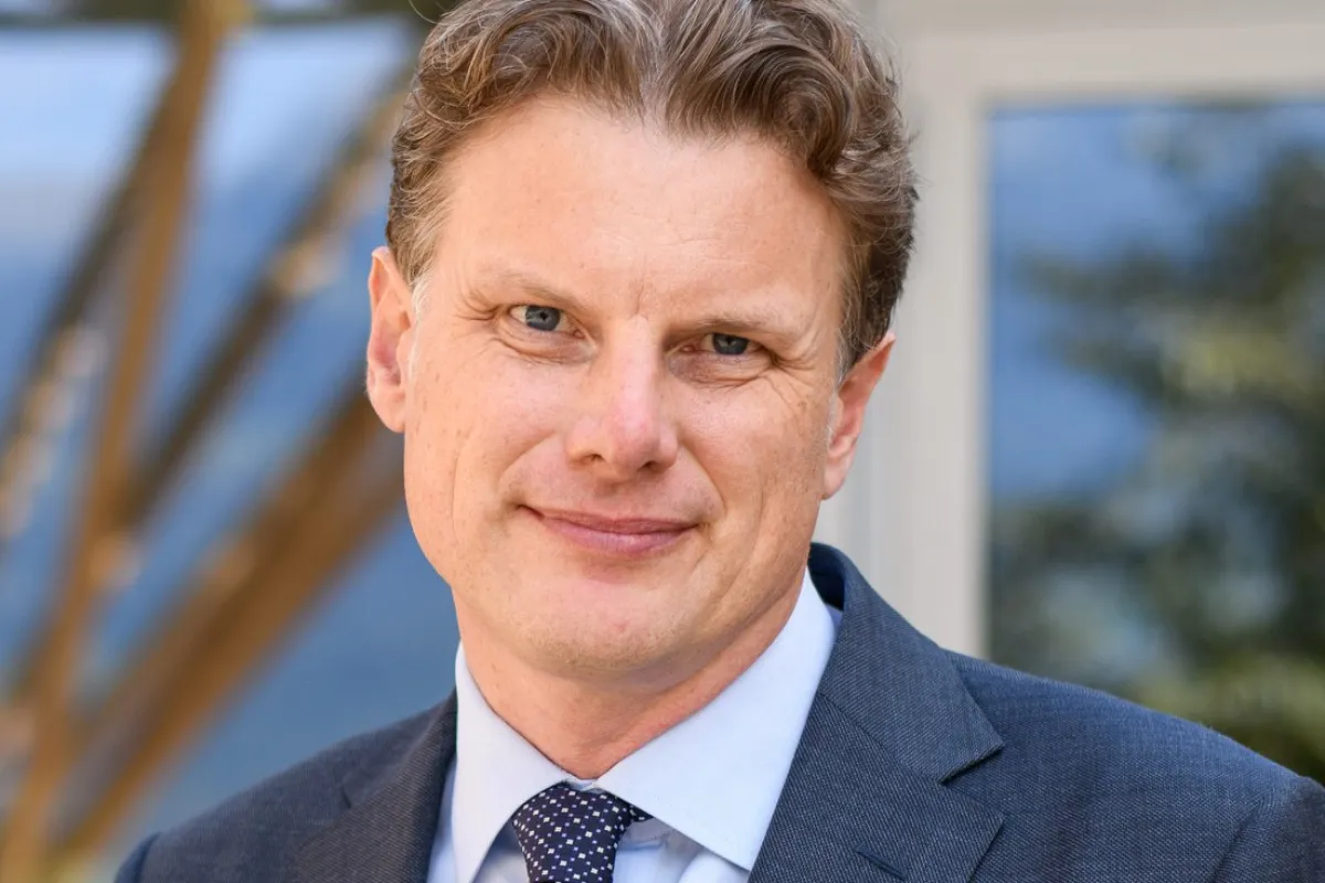 Ein Mann in einem Anzug steht lächelnd vor einem Gebäude.