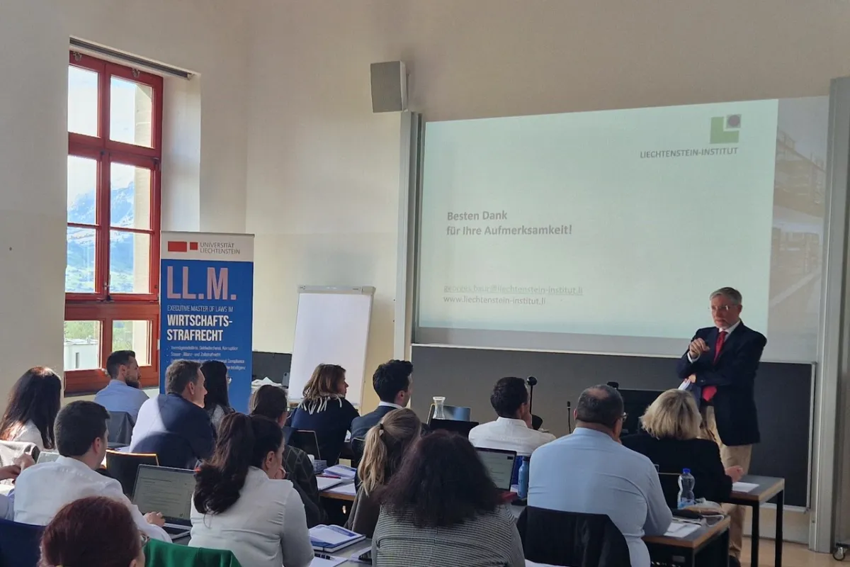 Ein Vortragender steht vor einer Gruppe von Teilnehmenden in einem Seminarraum der Universität Liechtenstein. Auf der Leinwand ist eine Präsentationsfolie mit dem Text "Besten Dank für Ihre Aufmerksamkeit!" zu sehen. Im Hintergrund ist ein Banner mit der Aufschrift "LL.M. Wirtschafts-Strafrecht" sichtbar.