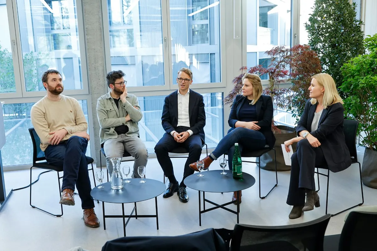Podiumsdiskussion an der Universität Liechtenstein: Fünf Personen sitzen in einem modernen Raum mit großen Fenstern und Pflanzen, diskutieren über den Wohnungsmarkt. Vor ihnen stehen Tische mit Wassergläsern und einer Flasche.