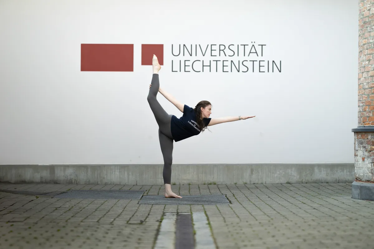 Frau in Sportkleidung übt Yoga-Pose vor Logo der Universität Liechtenstein.