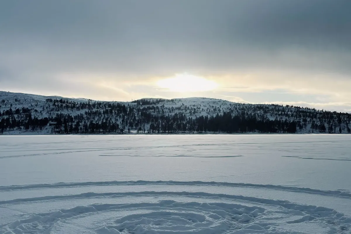 Spiralförmige Spur im Schnee auf gefrorenem See vor Hügeln.