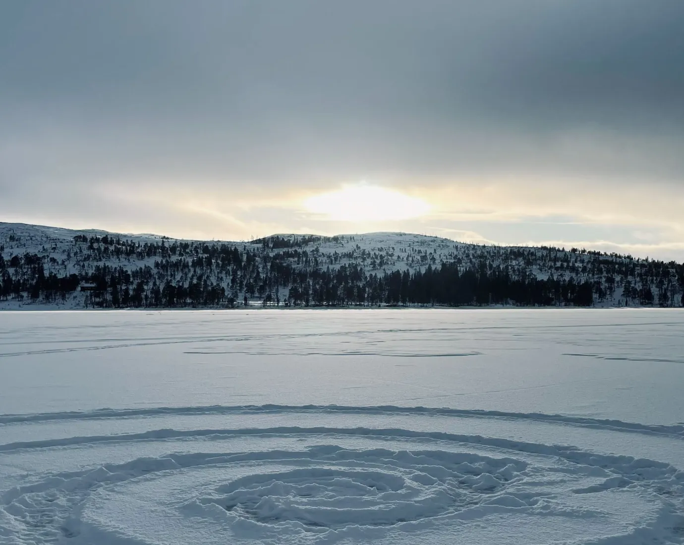 Spiralförmige Spur im Schnee auf gefrorenem See vor Hügeln.